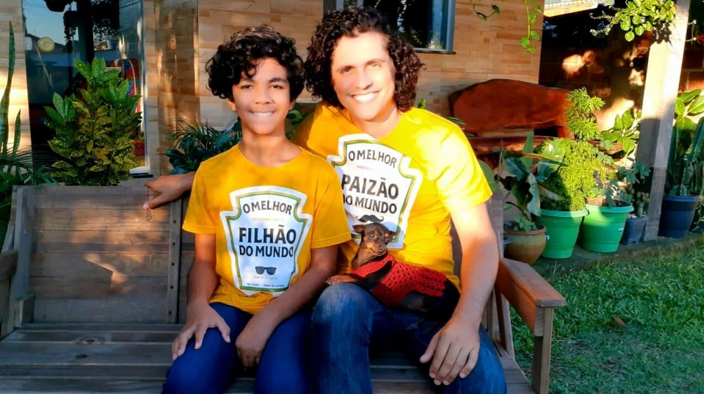 Pai e filho com camiseta combinando e cachorro no colo